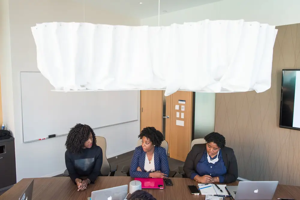 Three women in a bright office around a table with laptops and papers