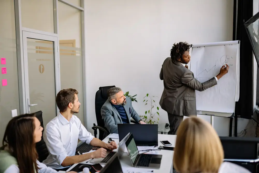 Colleagues gathered around a whiteboard in a bright office while one person sketches a plan